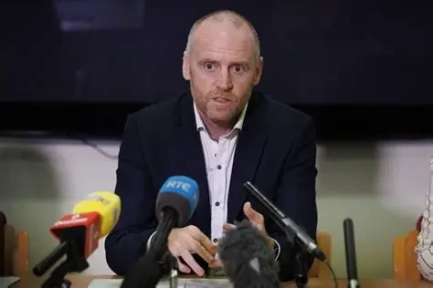 Press conference with microphones in the foreground, representing expert-led investigative review and public accountability.